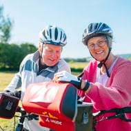 Zwei Radfahrer mit Helmen betrachten gemeinsam eine Karte auf ihren Rädern in ländlicher Gegend bei Hemeln, mit grünen Feldern und Bäumen im Hintergrund.