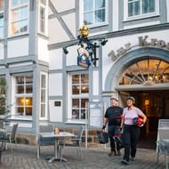 Zwei Radfahrer mit Helmen stehen vor dem Restaurant Zur Krone in Hamelns historischer Altstadt mit traditionellen Fachwerkhäusern.