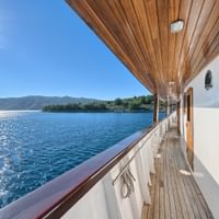 Holzdeck des Kreuzfahrtschiffs MY Magellan mit weißen Geländern und Kabinentüren, mit Blick auf blaue Adria und kroatische Küste.