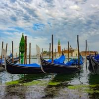 Traditionelle schwarze Gondeln mit blauen Planen an Holzpfählen in der Lagune von Venedig. San Giorgio Maggiore Kirche mit Glockenturm im Hintergrund.