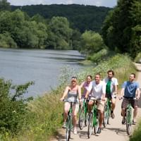 Gruppe von fünf Radfahrern mit Rädern auf gepflastertem Weg entlang der Lahn bei Villmar, umgeben von grünen Bäumen und Hügeln.