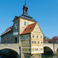 Bamberg's Old Town Hall with baroque tower and half-timbered facade built on stone bridge over river, surrounded by colorful historic buildings.