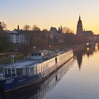 Flusskreuzfahrtschiff MS Casanova am Morgen mit historischer Stadtsilhouette und Kirchtürmen, die sich im ruhigen Wasser spiegeln.