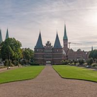 Das historische Holstentor in Lübeck mit seinen charakteristischen Zwillingstürmen und spitzen Türmen, gesehen über eine gepflegte Rasenfläche.