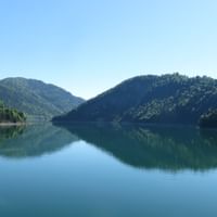 Sylvensteinsee Bergsee mit perfekter Spiegelung bewaldeter Hügel unter klarem blauen Himmel in Bayern, Deutschland.