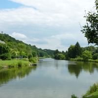 Ruhige Lahn mit grünen Wiesen und Bäumen an beiden Ufern. Häuser in der Ferne unter bewölktem Himmel mit blauen Stellen.