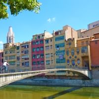 Radfahrer überquert die Prinzessinnenbrücke über den Fluss Onyar in Girona, mit bunten historischen Häusern am Flussufer und Kathedralturm.