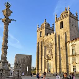 Historische Pelourinho-Steinsäule mit kunstvollen Schnitzereien vor den Zwillingstürmen und der Barockfassade der Kathedrale von Porto.
