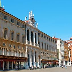 Historische Piazza dei Signori in Vicenza mit der Palladianischen Basilika mit weißen Säulen und Bögen, bunten Gebäuden und einem Denkmal.