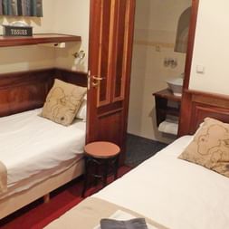 Doppelkabine auf Simmer fan Fryslan mit zwei Einzelbetten, Holzmöbeln, Zierkissen und Tür zum eigenen Badezimmer.