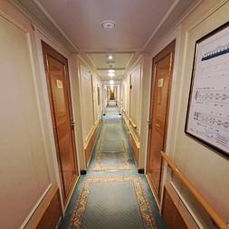 Langer Gang auf der MS Casanova mit Holzkabinentüren, cremefarbenen Wänden, dekorativem Teppichläufer und Handläufen an beiden Seiten.