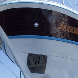 Nahaufnahme des weiß-blauen Bugs des Schiffes San Snova mit sichtbarem Namen auf dem dunklen Rumpf, Ankermechanismus und Takelage.