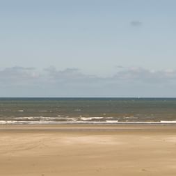 Weitläufiger Sandstrand auf Terschelling mit sanften Wellen, die an die Küste rollen, unter bewölktem Himmel. Der breite Strand erstreckt sich in die Ferne.