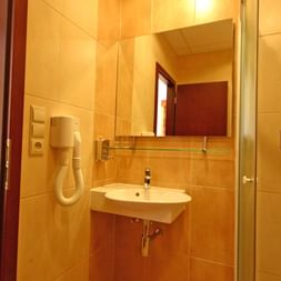 Modernes Badezimmer mit gelben Fliesen, Wandwaschbecken, Spiegel, Glasdusche mit Mosaikfliesen und Haartrockner im Hotel Ludmila in Mělník.