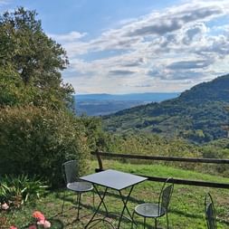 Außenterrasse in der Toskana mit Metalltisch und Stühlen mit Blick auf grüne Hügel und Täler unter bewölktem blauen Himmel.