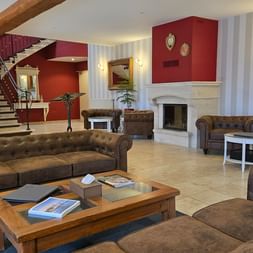 Spacious hotel lobby with brown leather sofas, fireplace, striped walls, and staircase. Warm lighting and potted plants create a welcoming atmosphere.
