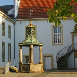 Innenhof des Falkenhof Museums mit weißen Gebäuden, roten Ziegeldächern, verziertem Brunnen mit goldener Kuppel und geschwungener Treppe.