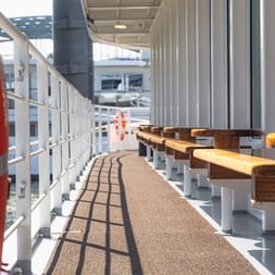 Ship deck of MS Lisabelle with orange life preserver in foreground, wooden benches along white railing, and covered walkway overhead.