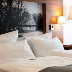 Helles Hotelzimmer im Hotel Zollhaus Rastede mit zwei Betten mit weißer Bettwäsche, Wandlampen und einem Schwarz-Weiß-Foto über dem Kopfteil.