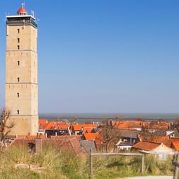 Hoher beiger Leuchtturm mit rotem Dach überragt das Dorf Terschelling mit traditionellen holländischen Häusern mit orangeroten Ziegeldächern.