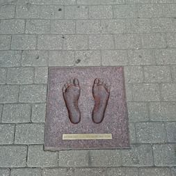 Bronzeplakette mit zwei Fußabdrücken im Kopfsteinpflaster der Rigaer Altstadt, mit kleiner Inschriftenplatte darunter.