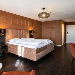 Modernes Hotelzimmer mit braunen Wänden, beigem Boxspringbett, dunklem Holzboden, korallenfarbenen Sesseln und mintgrüner Küchenzeile im Hotel Old Dutch Volendam.