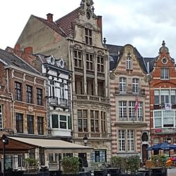 Reihe bunter mittelalterlicher Gildenhäuser mit verzierten Treppengiebeln in Brügge. Die Gebäude haben rote Backsteinfassaden, Steinverzierungen und Cafés im Erdgeschoss.