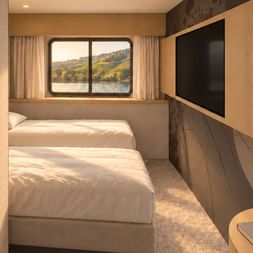 Modern cabin on MS Veloria with two single beds, wooden furniture, flat-screen TV, and window showing river landscape with hills.