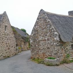 Traditionelle Steinhäuser in der Nordbretagne mit Reetdächern und Granitmauern. Blaue Fensterläden akzentuieren die rustikale Architektur.