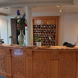 Eleganter Empfangsbereich auf der MS Casanova mit kunstvoll geschnitztem Holztresen, Marmorplatte, Schlüsselschrank und Blumenvase.