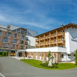 Moderner Alpiner Hotelkomplex mit traditionellen Holzbalkonen und zeitgenössischem Glasflügel, umgeben von grünen Rasenflächen.