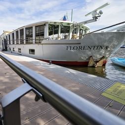 Weißes Flusskreuzfahrtschiff MS Florentina an einem Holzsteg vertäut. Das moderne Schiff verfügt über große Fenster und ein überdachtes Oberdeck.