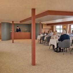Spacious restaurant aboard MS Veloria with white-clothed tables, gray upholstered chairs, and large windows overlooking the river landscape.