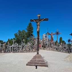Großes Kruzifix auf einem Weg am Berg der Kreuze in Litauen, mit Tausenden von Kreuzen und religiösen Skulpturen unter blauem Himmel.