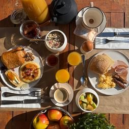 Breakfast table with croissants, bread rolls, scrambled eggs, sausages, fresh fruit, orange juice, coffee, muesli, and jam at Ceres Boutique Hotel.