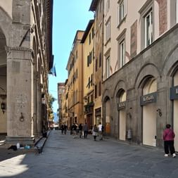 Fußgängerstraße in der Toskana mit mittelalterlichen Steingebäuden, Bogenfassaden und bunten mehrstöckigen Häusern. Menschen gehen auf Steinpflaster.