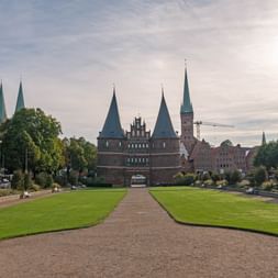 Das historische Holstentor in Lübeck mit seinen charakteristischen Zwillingstürmen und spitzen Türmen, gesehen über eine gepflegte Rasenfläche.