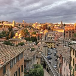 Umbrische Dächer bei Sonnenuntergang Panoramablick auf eine umbrische Hügelstadt mit Terrakotta-Dächern und historischen Gebäuden im goldenen Sonnenlicht unter dramatischem Himmel.
