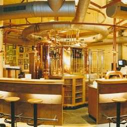 Runde Bar mit kupfernen Braukesseln im Hammerbräu. Barhocker umgeben die Theke mit sichtbarer Brauanlage und Kupferrohren darüber.