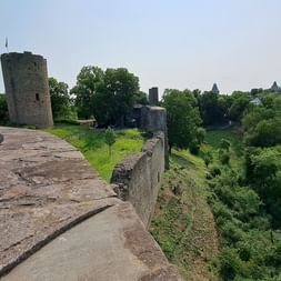 Steinmauern und Turm der Burg Blankenberg umgeben von grünen Bäumen. Ein Dorf ist auf dem Hügel in der Ferne sichtbar.