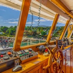 Schiffsbrücke der MY Linda mit Holzsteuerrad, Steuerpult und Panoramafenstern mit Blick auf kroatische Küste und Fahrräder an Deck.