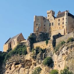 Mittelalterliches Steinschloss auf einer dramatischen Kalksteinklippe in der Dordogne mit Türmen und Gebäuden vor klarem blauen Himmel.