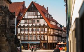 Traditionelle Fachwerkhäuser mit roten Ziegeldächern säumen einen historischen Platz in Hameln. Menschen gehen über das Kopfsteinpflaster.