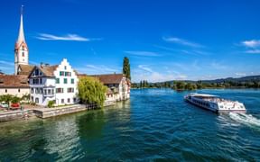 Weißes Passagierschiff auf dem Rhein vor Stein am Rhein mit mittelalterlichem Kirchturm, bunten Fachwerkhäusern und Uferpromenade.