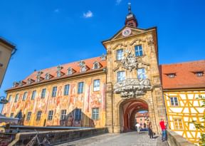 Bamberg's Old Town Hall with ornate frescoed facade and clock tower, built on a bridge over water with half-timbered buildings nearby.