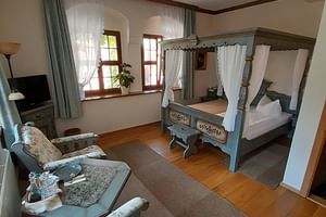 Geräumiges Hotelzimmer in Bautzen mit antikem blauen Himmelbett, blumig gepolsterten Sitzmöbeln, Holzboden und Bogenfenstern mit Vorhängen.