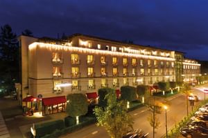 Außenansicht des Victors Residenz Hotels bei Nacht mit warmer Beleuchtung, mehreren Stockwerken mit beleuchteten Fenstern, roten Markisen.