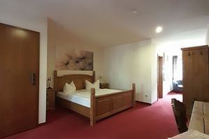 Geräumiges Hotelzimmer mit Holzdoppelbett, rotem Teppich, Holzmöbeln und Wandbild. Tür führt zum Nebenzimmer in der Schlossschänke Bautzen.