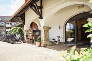 Hoteleingang mit weißem Bogenportikus, Holzbalken, Fahrradparkplatz und Außensitzbereich in Varel, Ostfriesland.