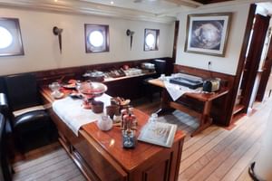 Schiffsspeisesaal mit Holztischen, Bänken und Buffetaufbau. Runde Bullaugen säumen die Wände mit nautischer Dekoration und gerahmten Kunstwerken.